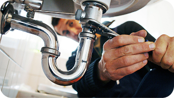 Technician working on plumbing pipes underneath a sink